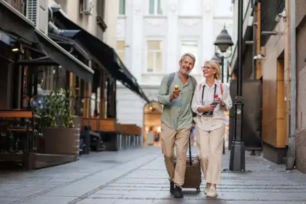 Happy couple in their fifties exploring a European city street with luggage