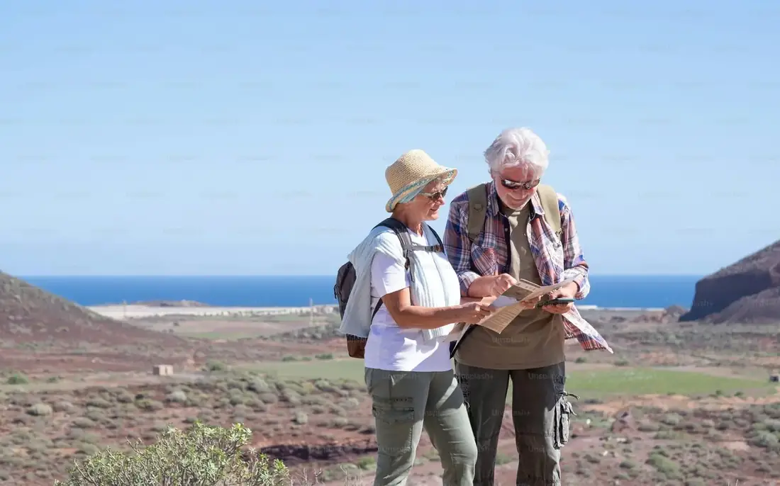Active senior couple with backpacks reading a map on a coastal mountain trail